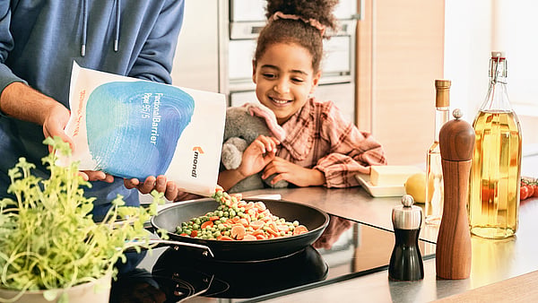 young girl sat at a kitchen table smiling and watching someone prepare food